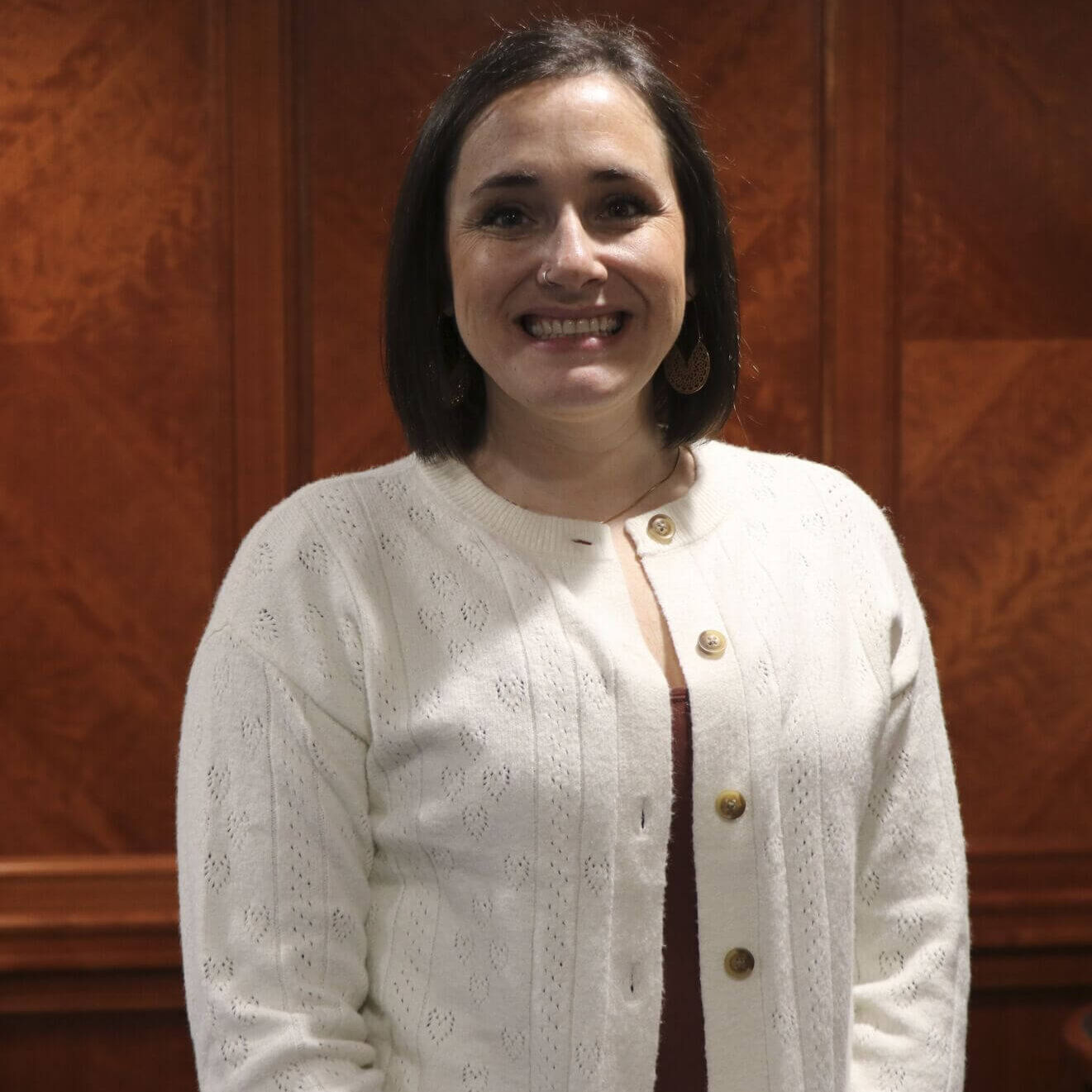 Professional headshot of Amber Butterfield, Executive Coordinator for the Michigan Association of Conservation Districts (MACD). She is wearing a cream cardigan and smiling against a wood-paneled indoor background.