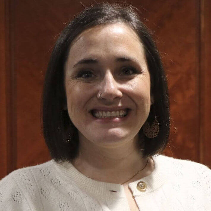 Professional headshot of Amber Butterfield, Executive Coordinator for the Michigan Association of Conservation Districts (MACD). She is wearing a cream cardigan and smiling against a wood-paneled indoor background.