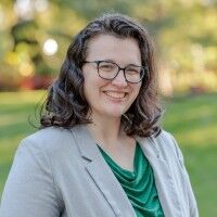 Professional headshot of Rivka Hodgkinson, Executive Director of the Michigan Association of Conservation Districts (MACD). She is wearing a grey blazer and smiling against a natural outdoor background.