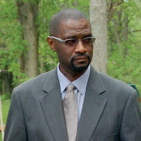 Albert Jones, NRCS Area 4 Conservationist, in a professional headshot wearing a grey suit and patterned tie with a natural forest background.